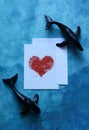 a card with a watercolor heart framed by toy whales on a blue watercolor background