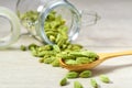 Cardamom pods in wooden scoop and in glass storage jar on a white wooden table, selective focus Royalty Free Stock Photo