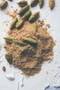 Cardamom powder or elaichi powder in bowl over moody background with pods.