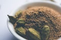 Cardamom powder or elaichi powder in bowl over moody background with pods.