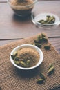 Cardamom powder or elaichi powder in bowl over moody background with pods.