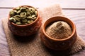 Cardamom powder or elaichi powder in bowl over moody background with pods.