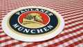 Cardboard beer coaster with Paulaner Munich logo on a checkered tablecloth