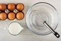 Cardboard box with eggs, jug of milk, whisk in bowl on wooden table. Top view Royalty Free Stock Photo