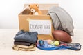 Cardboard box with donation clothes and different objects on white