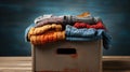 cardboard box filled with a jumble of old clothes, ranging from striped t-shirts to faded jeans and crumpled skirts. dec