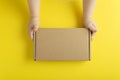 Cardboard box in small childrens hands. Yellow background top view. Mock up