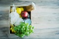 Cardboard box with various essentials, cereals, canned food, pasta, bananas, apples on a wooden table. Place for text