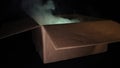 A cardboard box from which smoke comes and light shines. Concept of sorcery and magic. Black background