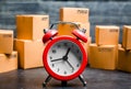 Cardboard boxes and red alarm clock. Time of delivery. Limited supply, shortage of goods in stock, hype and consumer fever. Time Royalty Free Stock Photo