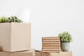 Cardboard boxes of things are stacked on the floor against a white wall. Books and table lamps and green plants in pots Royalty Free Stock Photo