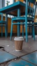 Cardboard coffee cup sits on a tiled floor near a blue table and chairs. Royalty Free Stock Photo