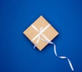 Cardboard gift square box tied with a white thin ribbon on a dark blue background