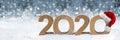 Cardboard number 2020 with red white santa claus hat in snow front of bright silver bokeh wooden background. Christmas and new Royalty Free Stock Photo