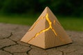 A cardboard pyramid with cracks and an inner golden light on the ground. Royalty Free Stock Photo