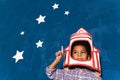 Cardboard rocket helmet on afro-american kid boy and stars on blue background.