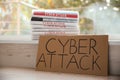 Cardboard with words CYBER ATTACK and newspapers on window sill, closeup Royalty Free Stock Photo