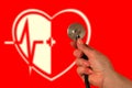 Cardio therapy concept. Hand with stethoscope on red background. Blurred image of heart, medical cross and electrocardiogram.