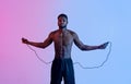 Cardio workout. Portrait of millennial black sportsman jumping on skipping rope in neon lighting Royalty Free Stock Photo