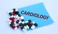 CARDIOLOGY word on a blue sheet of paper against the background of multicolored tablets