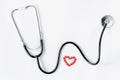 Cardiovascular system. Stethoscope and red pills in a heart shape on white background. Copy space. Royalty Free Stock Photo