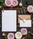 Cards and envelope between pink and cream roses on brown wood top view, wedding mockup Royalty Free Stock Photo