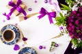 Cards and flowers, box gift, violet ribbon, morning cup coffee and cloth lying on a white table. Royalty Free Stock Photo