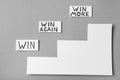 Cards with words WIN, WIN AGAIN, WIN MORE and paper cutout stairs on grey background, top view Royalty Free Stock Photo