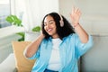 Carefree african american obese lady listening to music in wireless headphones and dancing on couch in living room Royalty Free Stock Photo