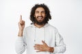 Carefree arab man laughing, pointing finger up and smiling, showing smth funny, standing in hoodie over white background