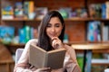 Carefree arab woman reading favorite book while sitting alone in cafe during daytime, after quarantine time, free space