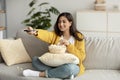 Carefree arab woman sitting on sofa with TV remote, choosing movie to watch and eating popcorn, free space