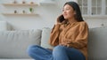 Carefree Asian woman talk mobile phone on couch in kitchen chinese korean japanese girl businesswoman call smartphone Royalty Free Stock Photo