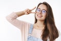 Carefree attactive young charismatic 20s woman in glasses with brown hair showing victory or peace gesture near face