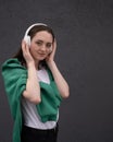 Carefree attractive brunette girl, dressed in a gray sweater, listening to music on headphones, standing on a gray background