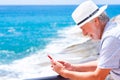 Carefree beautiful senior man using mobile phone at the sea. Happy retirement. Horizon over the water