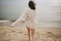 Carefree beautiful woman in knitted sweater and with windy hair running on sandy beach at cold sea, having fun. Stylish young Royalty Free Stock Photo