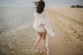 Carefree beautiful woman in knitted sweater and with windy hair running on sandy beach at cold sea, having fun. Stylish young sexy Royalty Free Stock Photo