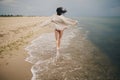 Carefree beautiful woman in knitted sweater and with windy hair running on sandy beach at cold sea, having fun. Stylish young sexy Royalty Free Stock Photo