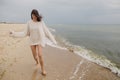 Carefree beautiful woman in knitted sweater and with windy hair running on sandy beach at cold sea waves, having fun. Stylish Royalty Free Stock Photo