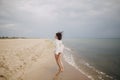 Carefree beautiful woman in knitted sweater and with windy hair running on sandy beach at cold sea waves, having fun. Stylish Royalty Free Stock Photo