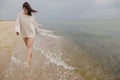 Carefree beautiful woman in knitted sweater and with windy hair running on sandy beach at cold sea waves, having fun. Stylish Royalty Free Stock Photo