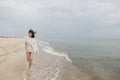 Carefree beautiful woman with windy hair running on sandy beach at cold sea waves, having fun. Stylish young happy female in Royalty Free Stock Photo