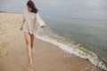 Carefree beautiful woman with windy hair running on sandy beach at cold sea waves, having fun. Stylish young happy female in Royalty Free Stock Photo