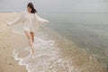 Carefree beautiful woman with windy hair running on sandy beach at cold sea waves, having fun. Stylish young happy female in Royalty Free Stock Photo