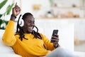 Carefree Black Guy Relaxing On Couch With Smartphone And Wireless Headphones Royalty Free Stock Photo