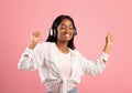 Carefree black woman in headphones dacing to her favorite music with closed eyes on pink studio background