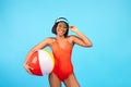 Carefree black woman in swimsuit posing with inflatable beach ball, smiling and looking at camera on blue background Royalty Free Stock Photo