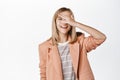 Carefree blond girl, little child student in blazer, smiling and laughing, touching face, standing in suit over white Royalty Free Stock Photo