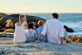 Carefree caucasian family watching the sunset sitting on a rock together on the beach. Parents spending time with their Royalty Free Stock Photo